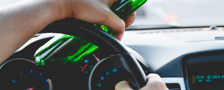 person holding an opened beer bottle while driving behind the wheel