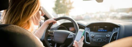 mujer al volante usando y mirando su teléfono móvil