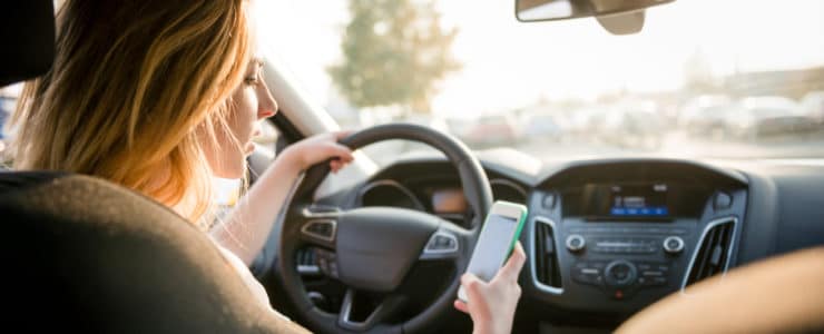 woman behind the wheel using and looking at her mobile phone
